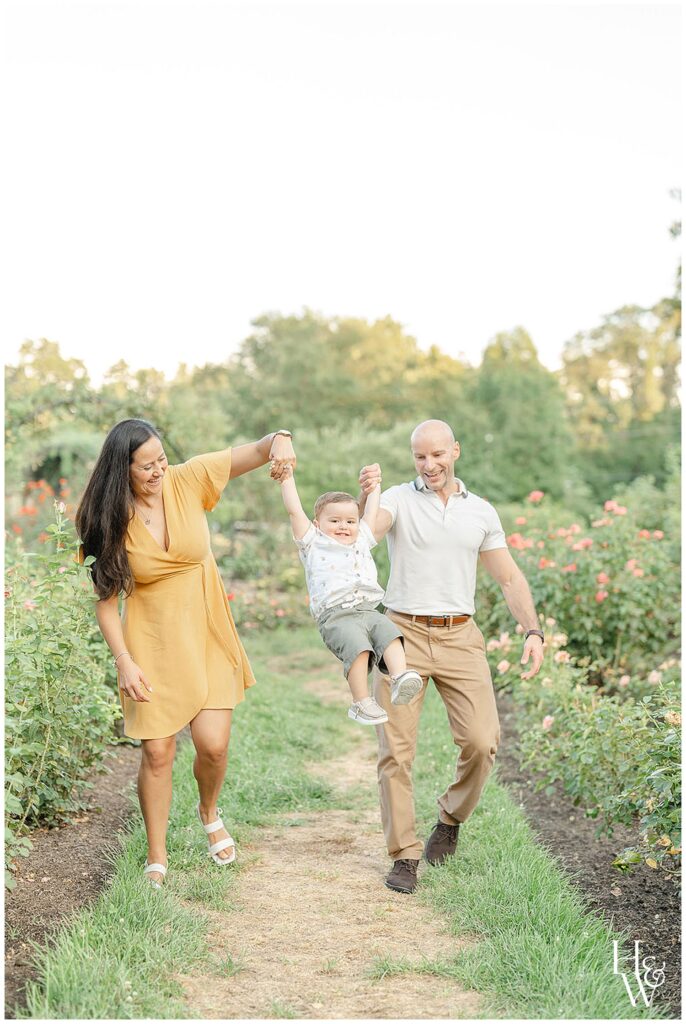 Parents swinging their toddler while walking through a garden path